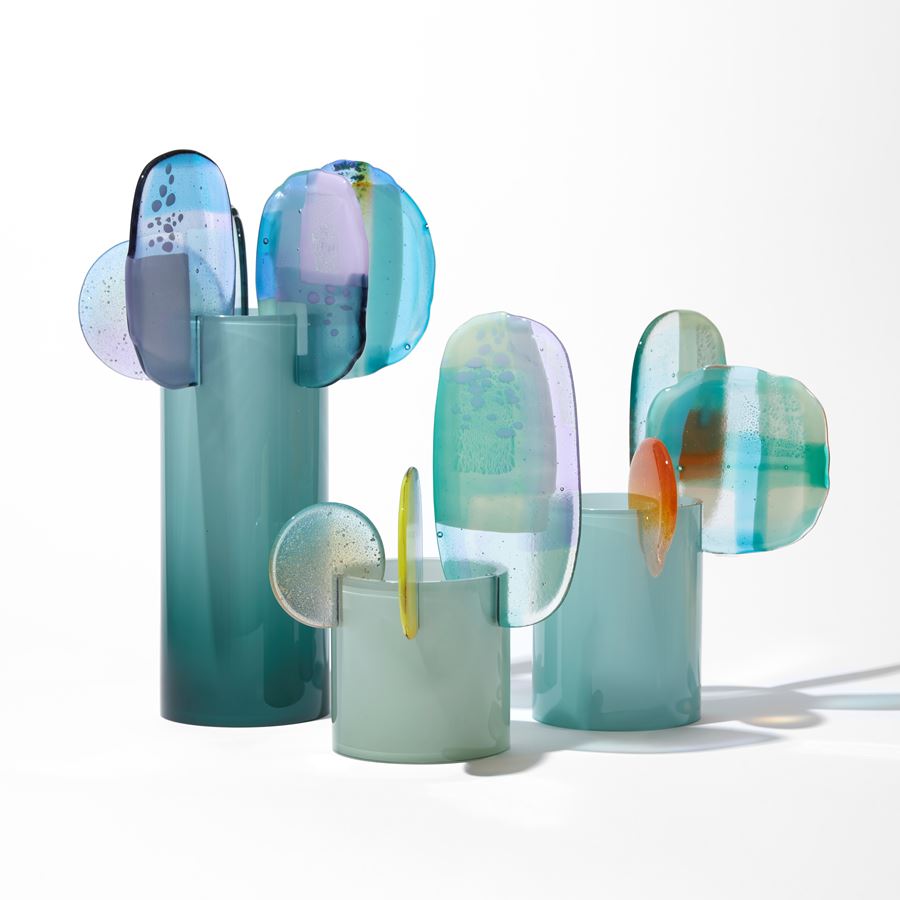 opaque teal cylinder with five rounded finials overlapping and perched on the top rim with abstract patterns in blue aqua jade turquoise lilac grey and yellow hand made from blown and fused glass